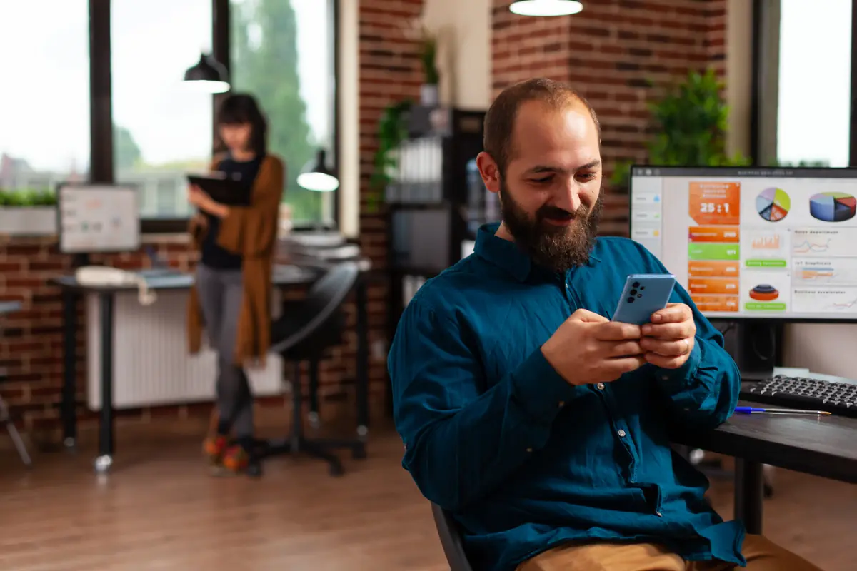 Ofiste telefonundan Instagram reklam sonuçlarını kontrol eden işletme sahibi, arkada rapor ekranı